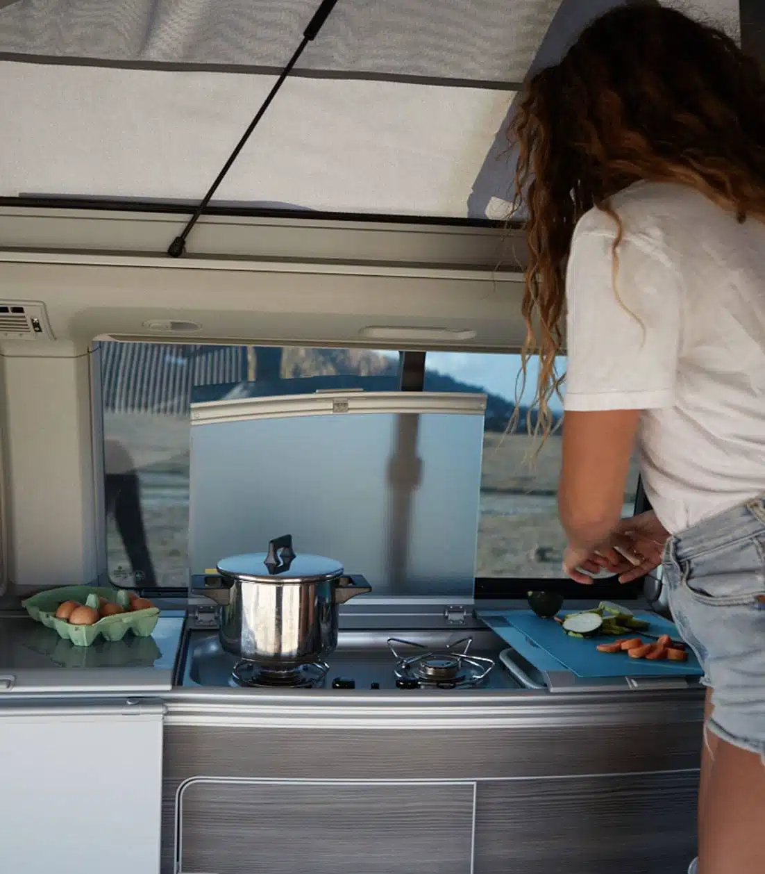 Woman cooking vegetables inside a campervan kitchenette