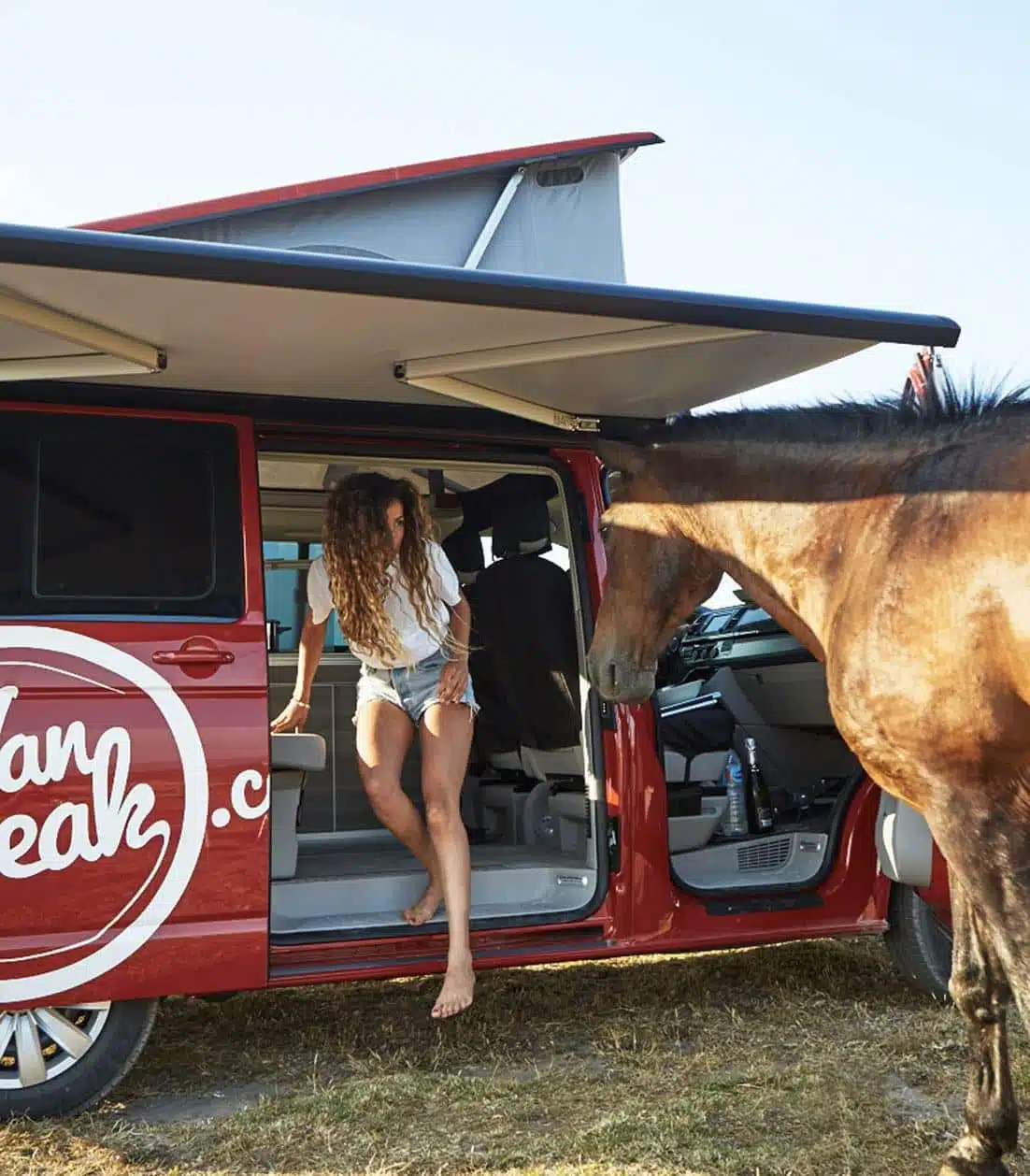 Woman stepping out of a red campervan in front of a horse