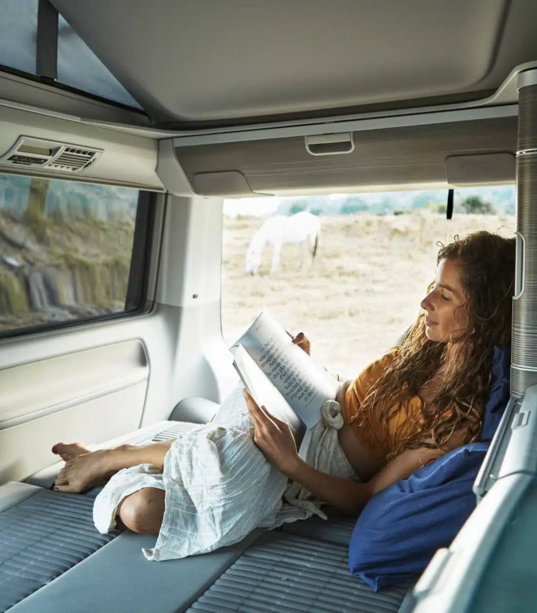 Curly haired woman reading inside a campervan
