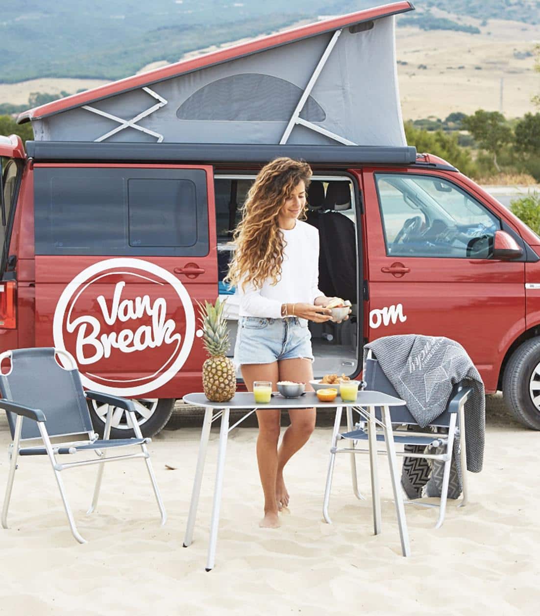 Curly haired woman setting up a table next to a red campervan VW